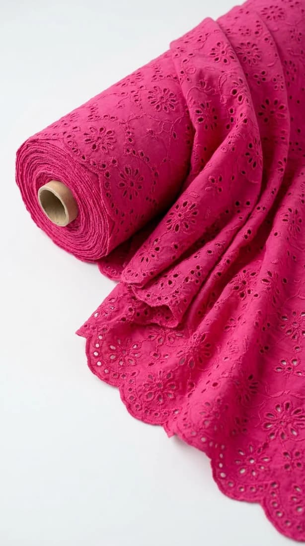 Roll of fuchsia schiffli eyelet fabric with a scalloped edge