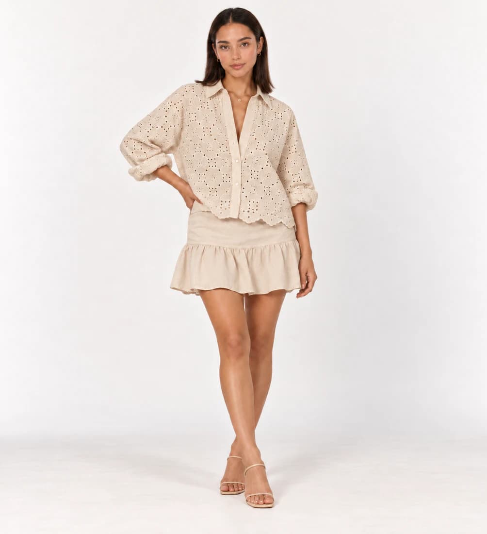 Model in an ivory eyelet shirt with a beige ruffled mini skirt