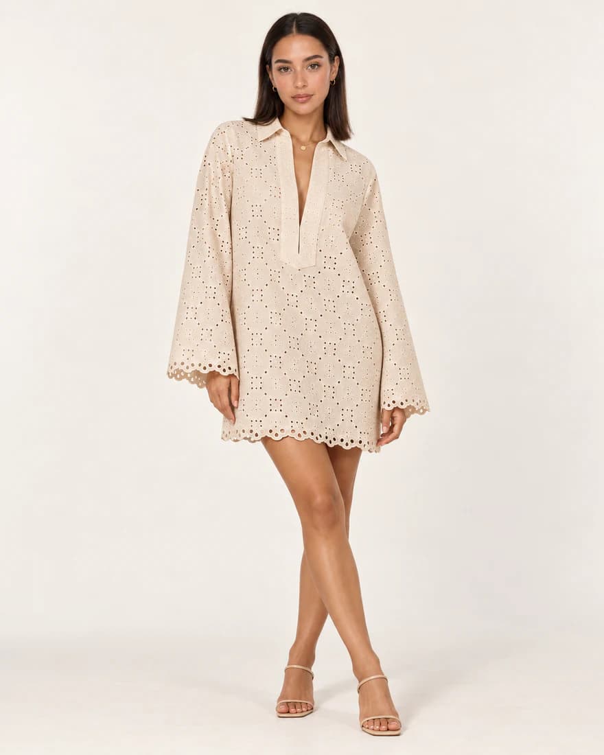 Model in an ivory eyelet tunic dress with flared sleeves and scalloped hems