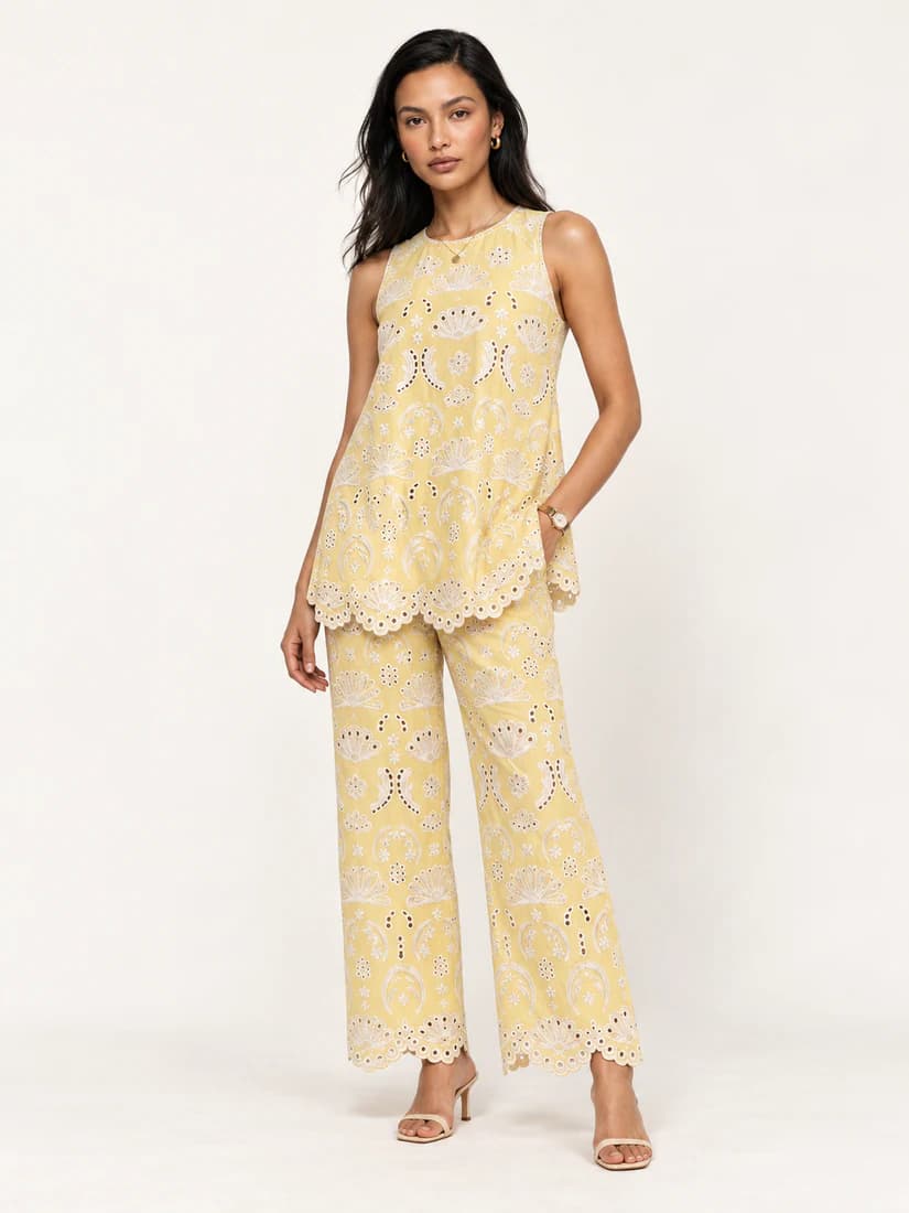 Model in a pale yellow embroidered sleeveless top and matching trousers with scalloped hems
