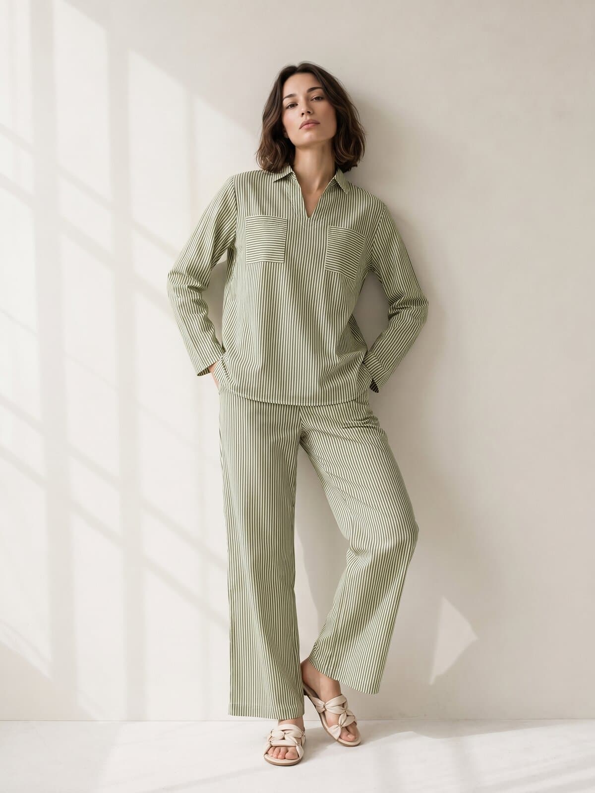 Olli on-model shot of the same pinstripe co-ord set, worn by a model leaning against a sunlit cream wall