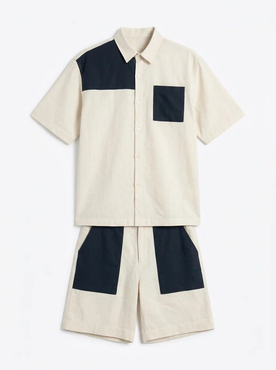 Flat lay of a men's cream linen co-ord set, a short-sleeve shirt with a navy shoulder yoke and navy chest pocket and shorts with navy front pocket panels, on a white background