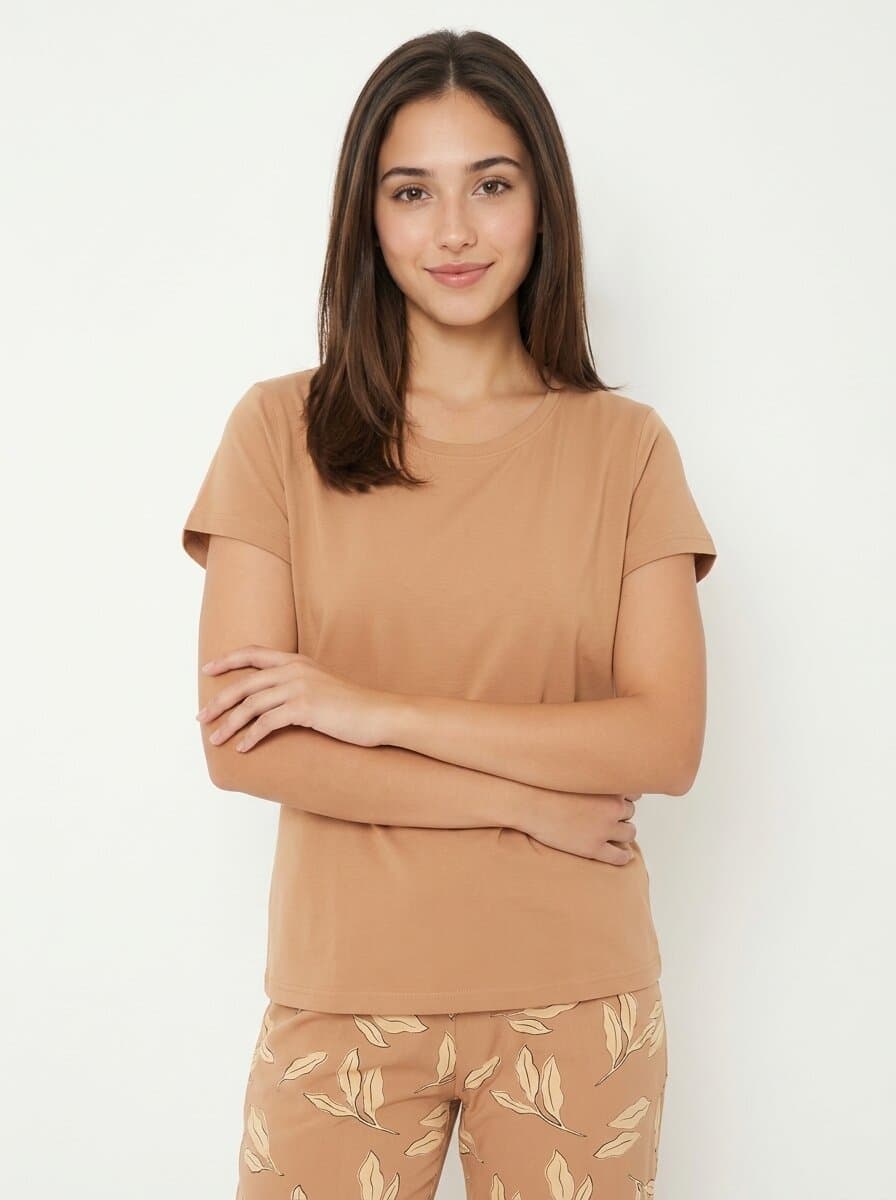 Studio shot of a women's tan crew-neck tee and matching leaf-print pyjama pants, worn by a model with folded arms against a plain off-white backdrop