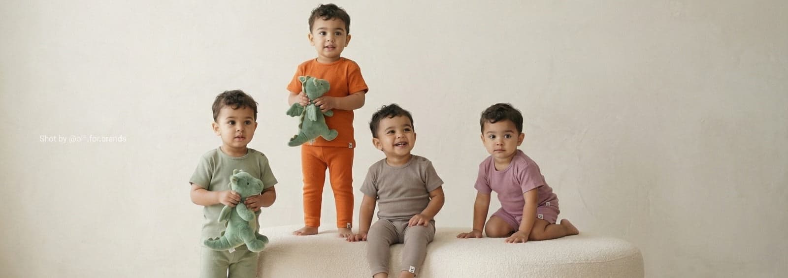 Kidswear banner with four children in coordinated outfits on a neutral set.